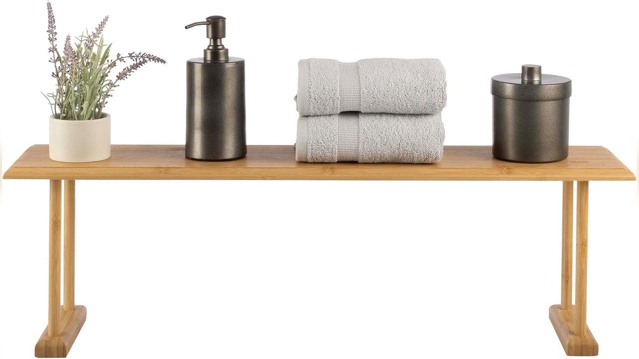 Natural bamboo shelf standing on a bathroom counter holding a soap pump, folded towels and a lavender plant