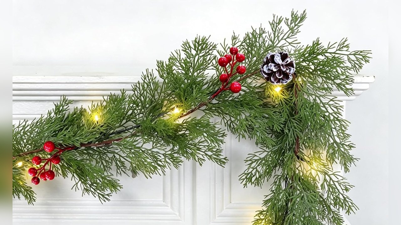 Pre-lit cedar garland with red berries and pinecones draped across a white mantel