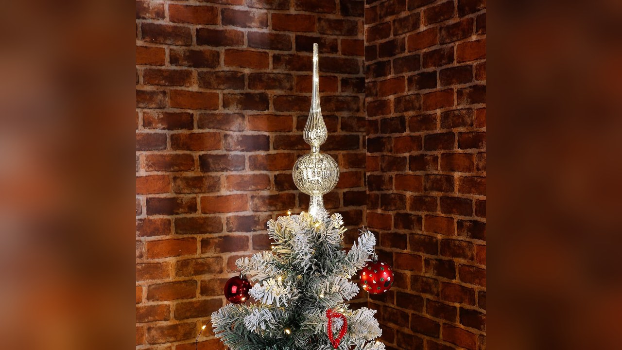 Silver mercury glass finial Christmas tree topper on a small flocked tree against a brick wall, christmas tree topper ideas