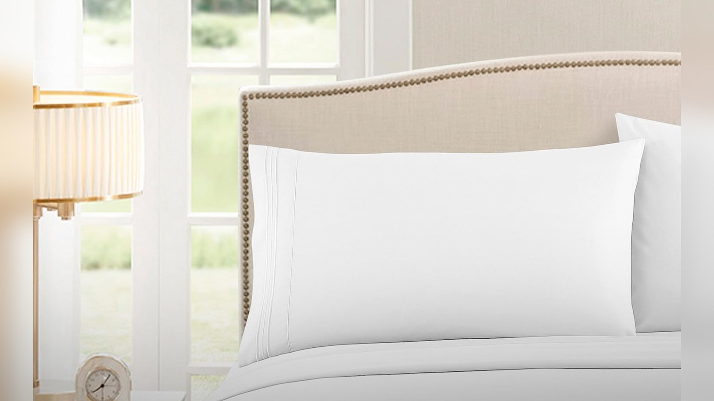 White deep pocket sheet set and pillowcase on a bed with an upholstered headboard