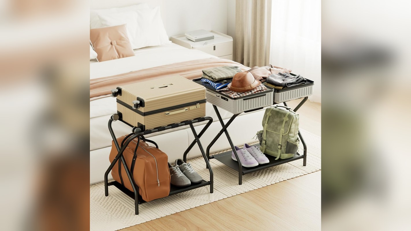 Two folding luggage racks holding open suitcases beside a guest bed