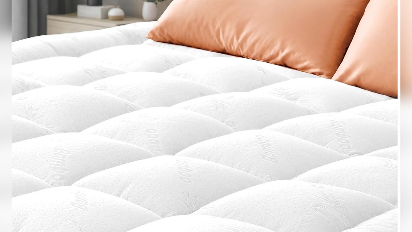 Quilted white mattress topper on a bed with orange pillows