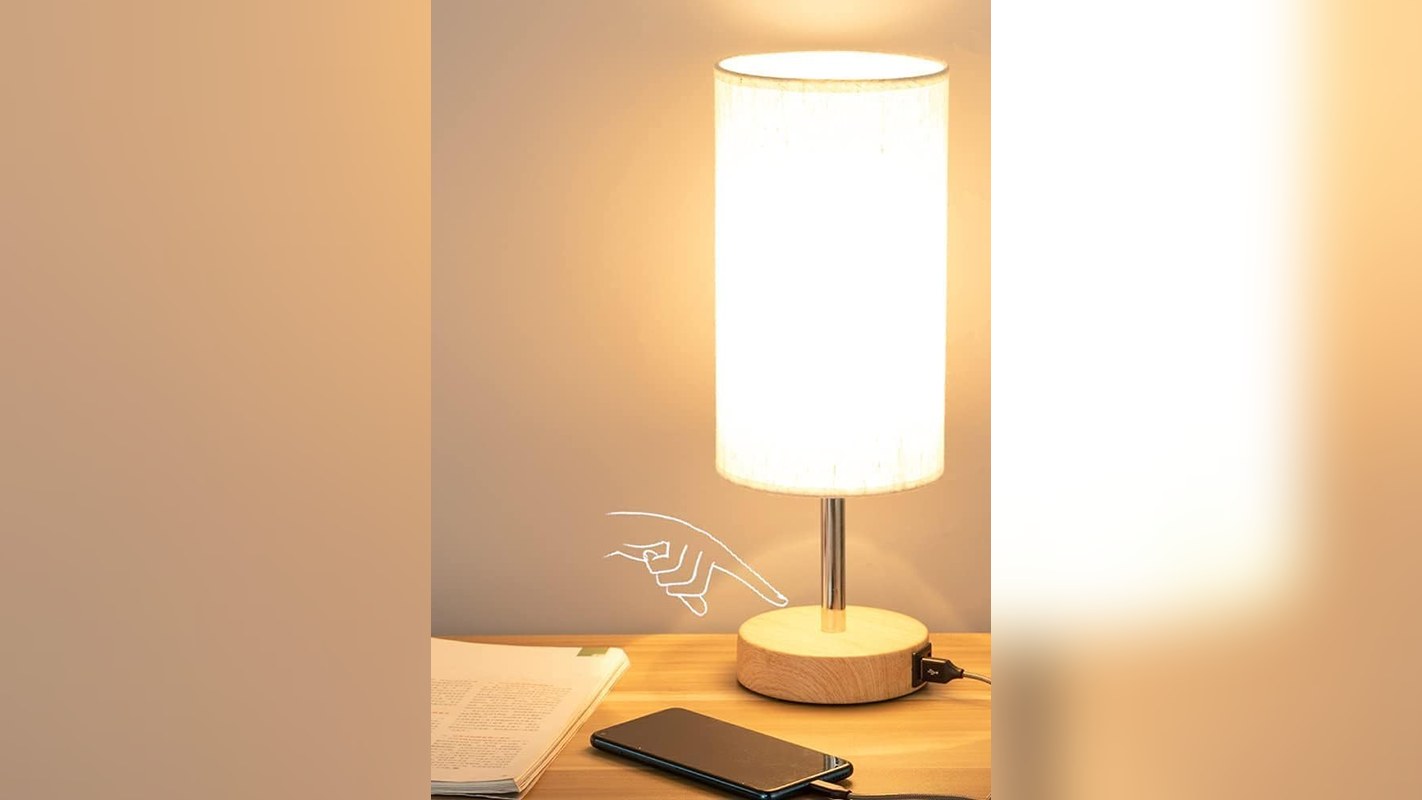 Touch dimmable bedside lamp glowing on a nightstand with a phone charging