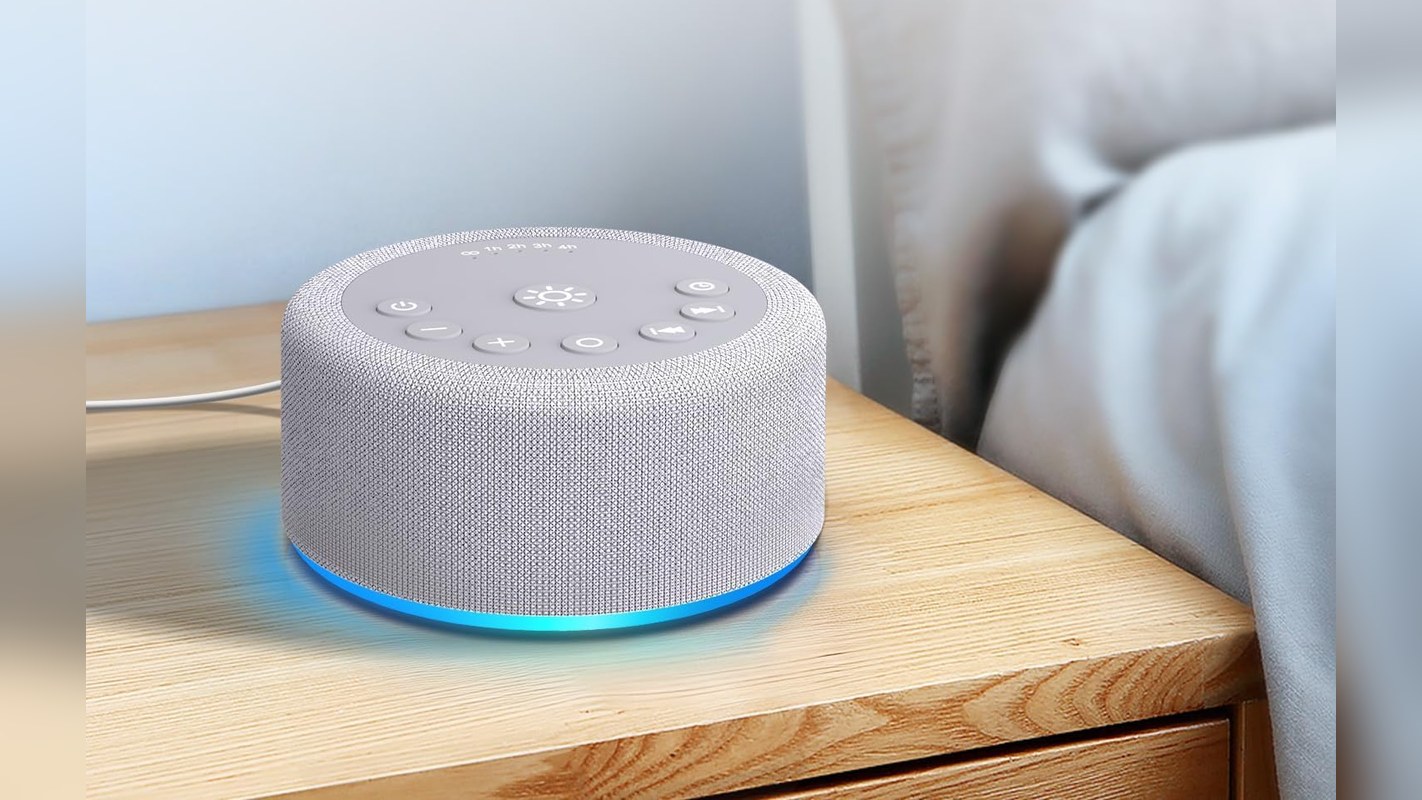 White noise machine with a night light glowing on a wooden nightstand
