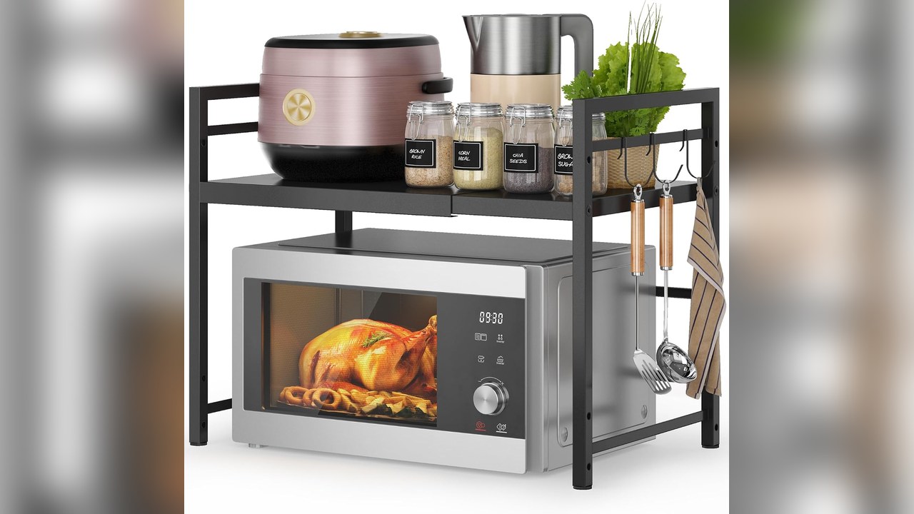 Black two tier expandable microwave oven rack on a kitchen counter holding appliances and jars