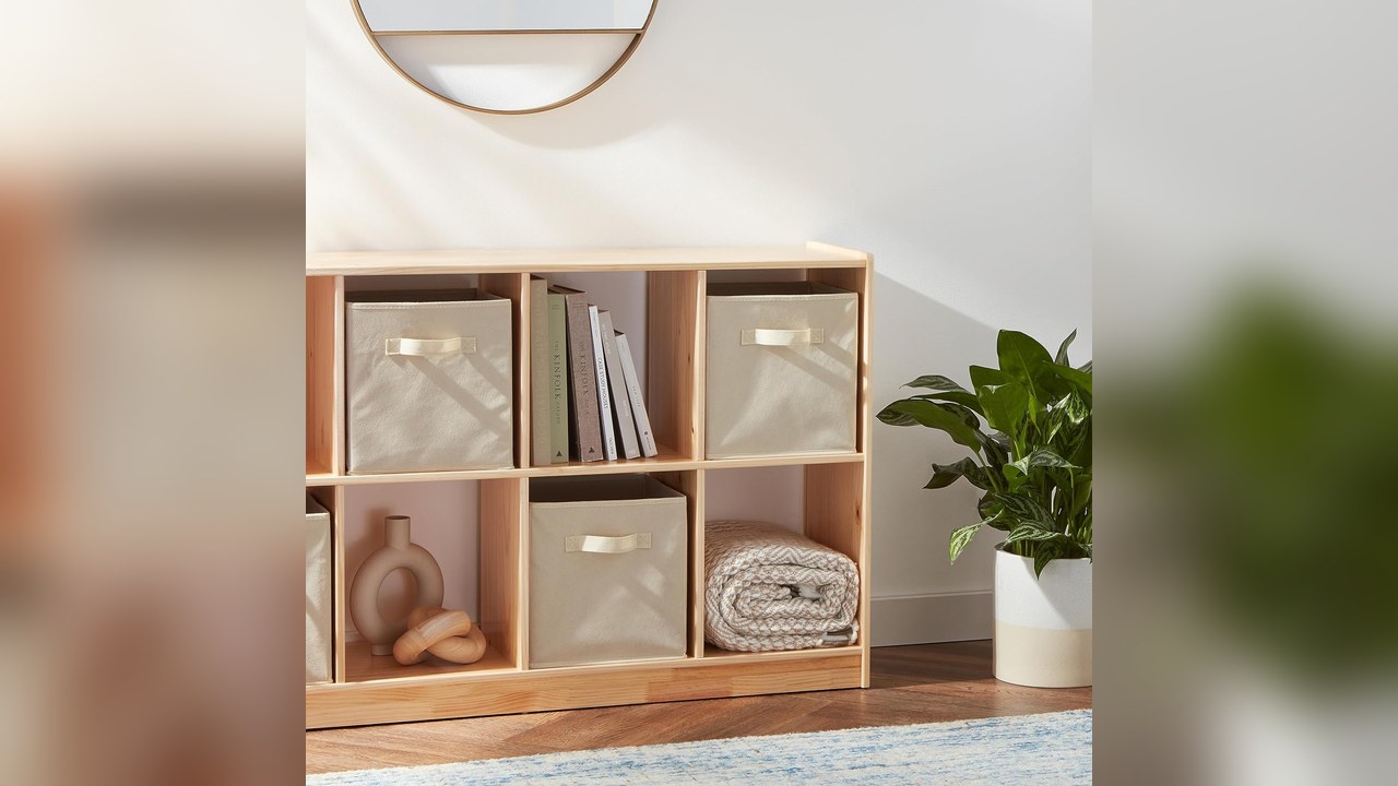 Beige collapsible fabric storage cubes with handles sitting in an open cube shelf next to books and a plant