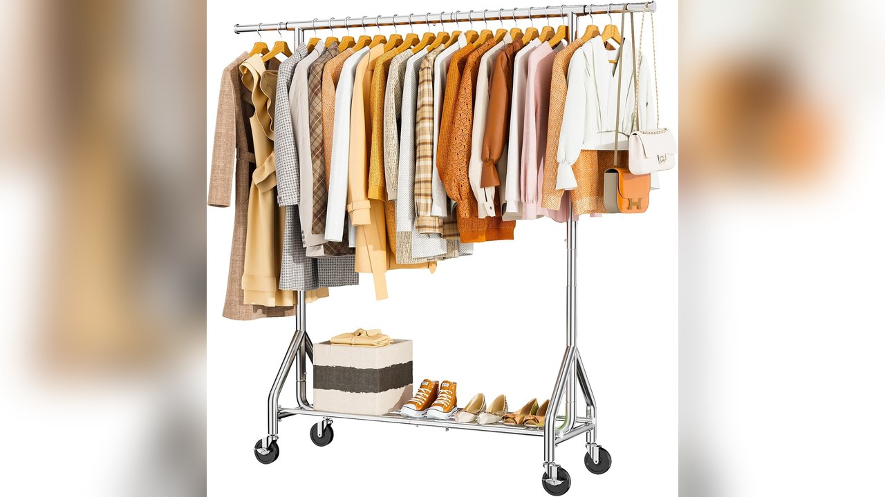 Silver rolling clothes rack with hanging clothes and a bottom shelf for shoes and a bag in a bedroom