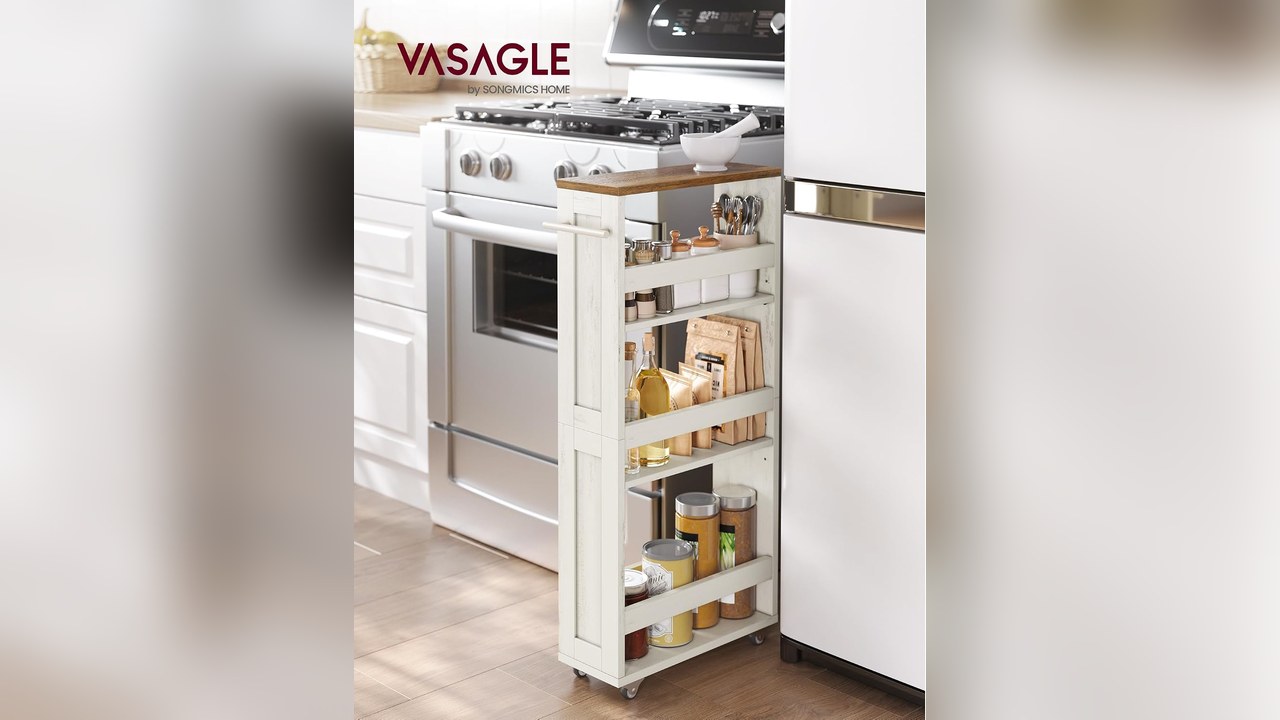 Slim white four-tier rolling cart with a wood top slid next to a stove and refrigerator, holding spices, oils and packaged food