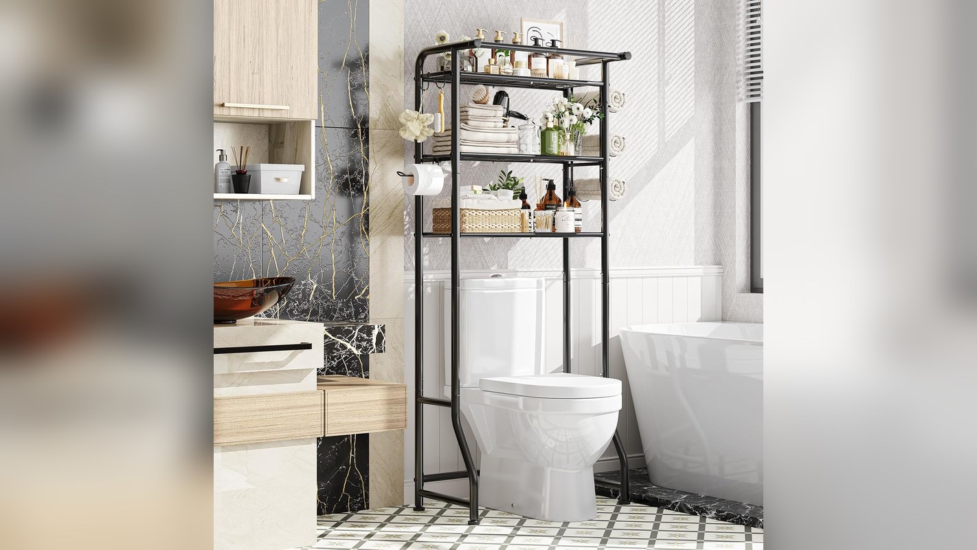 Black over-the-toilet storage shelf holding folded towels, baskets and toiletries in a bathroom