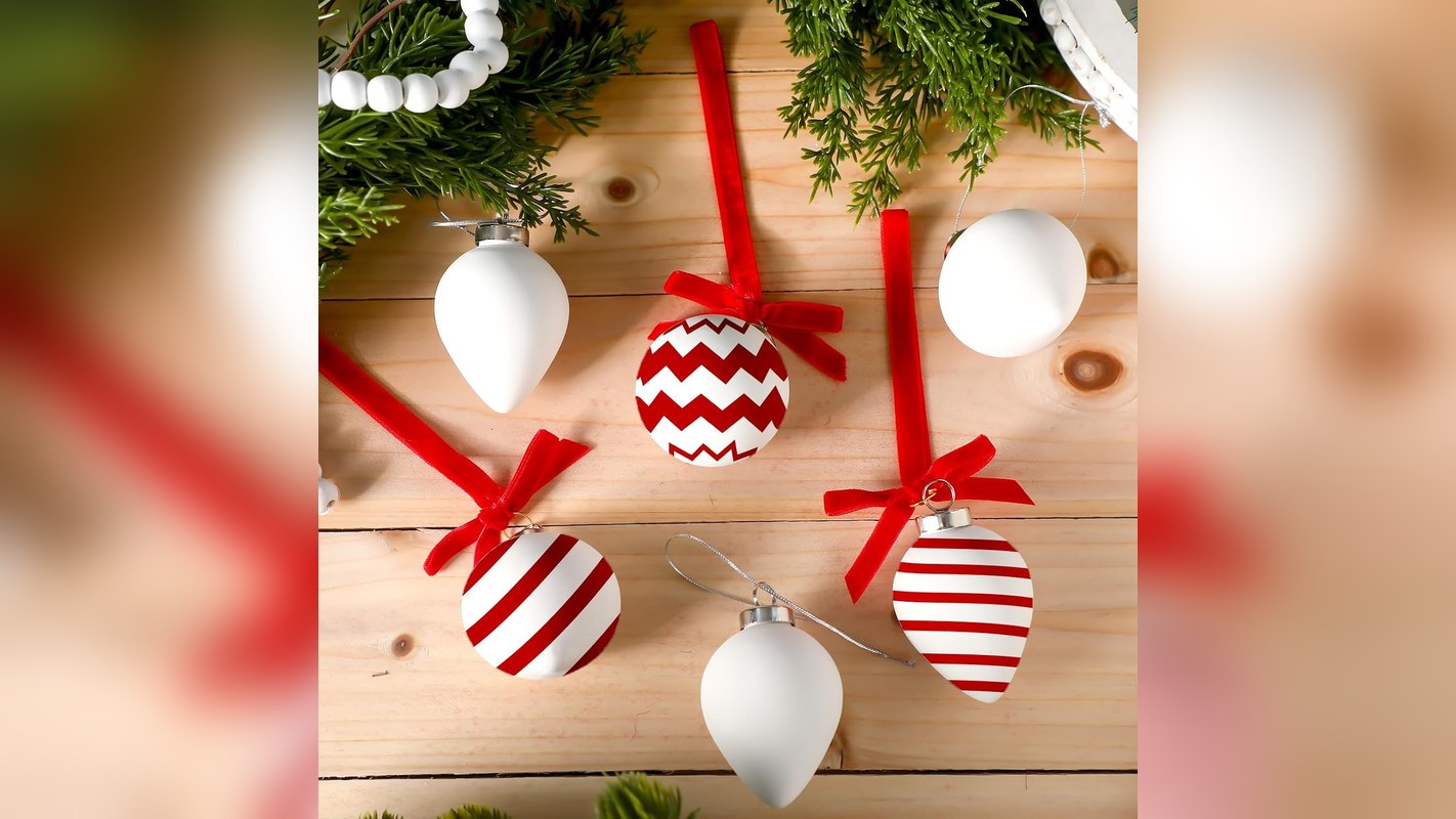 White blank ceramic ornaments with red velvet ribbons and painted stripes on a wooden table