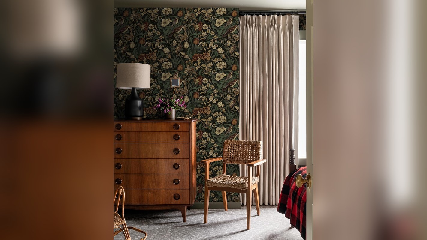 Dark floral peel-and-stick wallpaper behind a wooden dresser and lamp