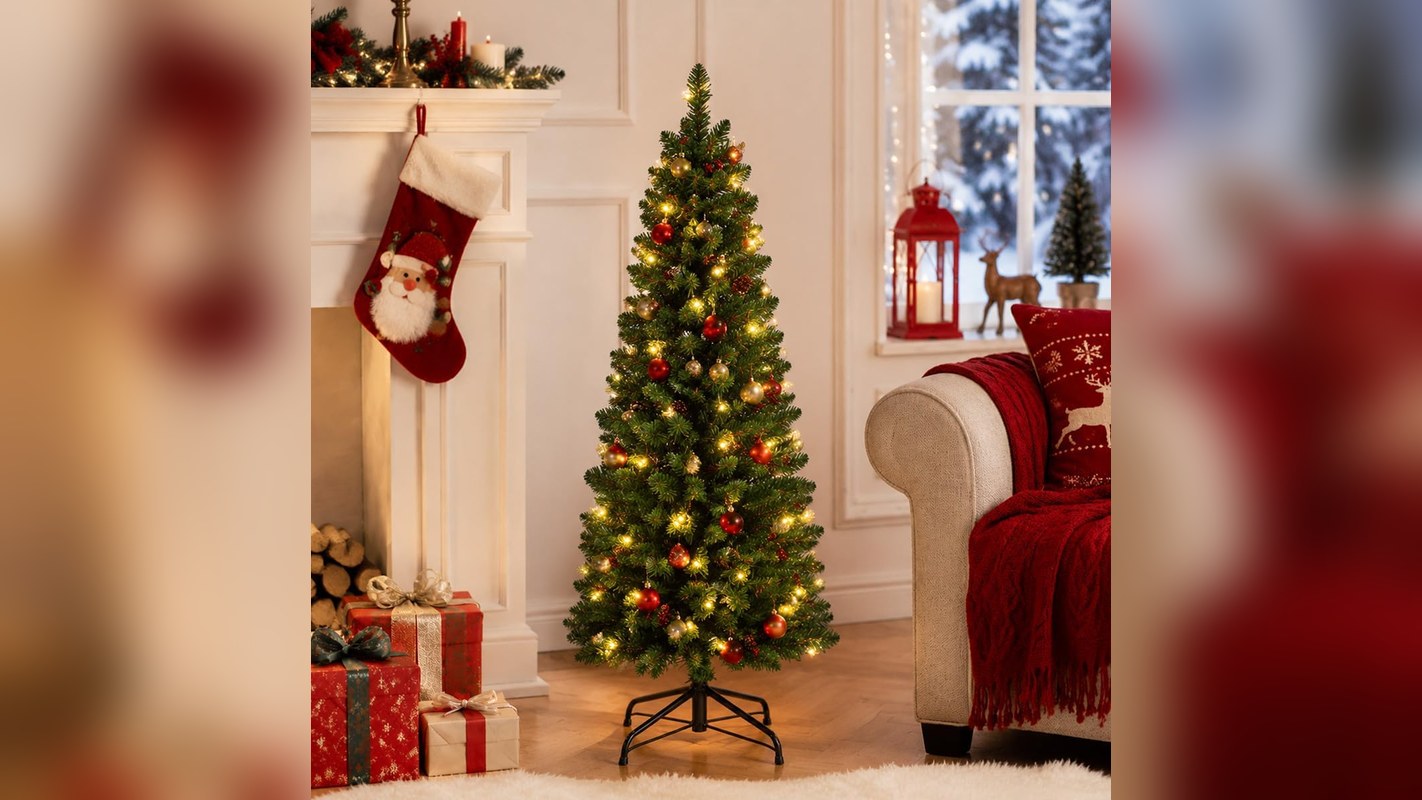 Slim pre-lit pencil Christmas tree next to a fireplace and sofa in a small apartment living room