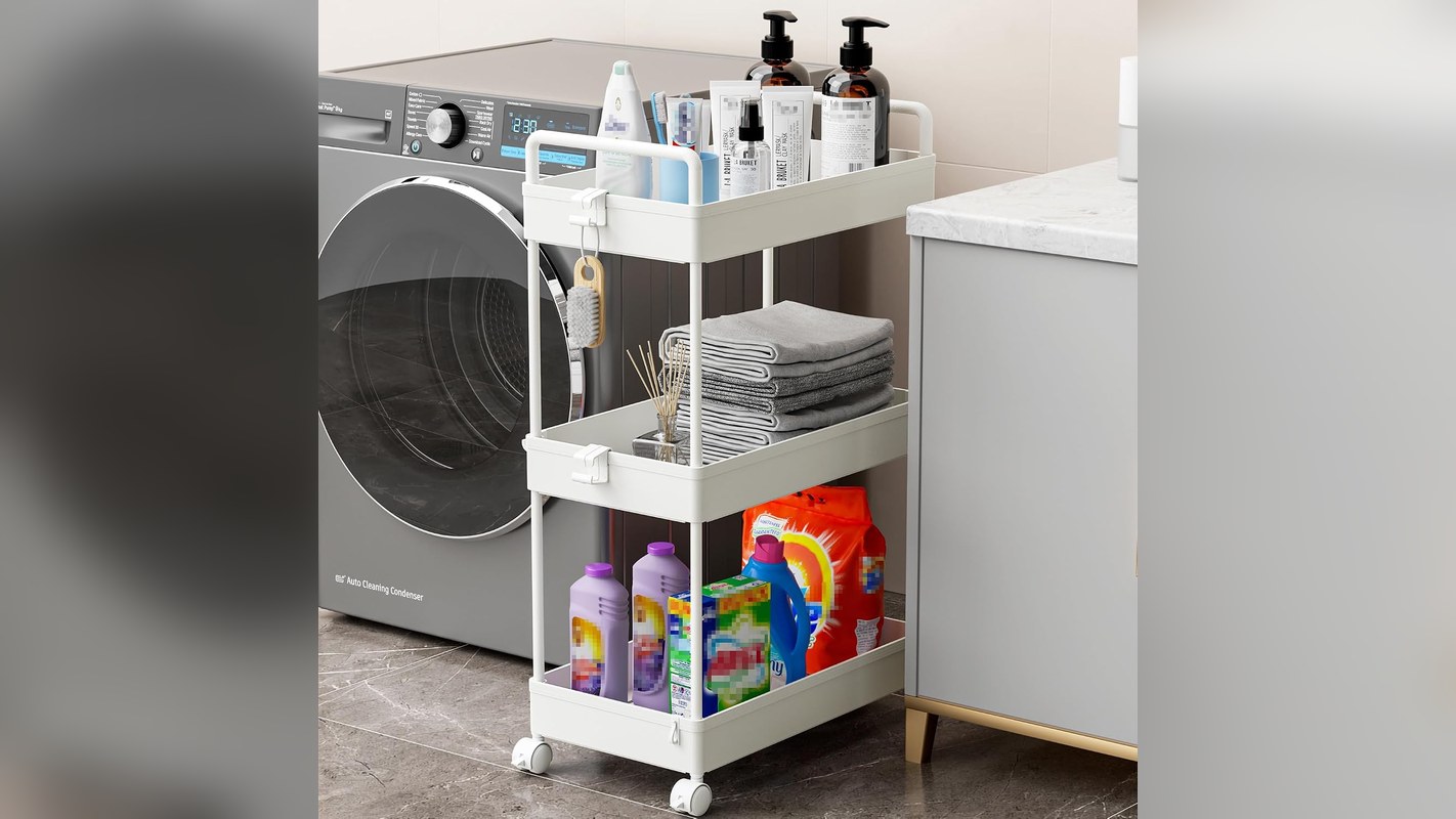 White slim rolling storage cart beside a washing machine holding folded towels and laundry supplies in a narrow gap