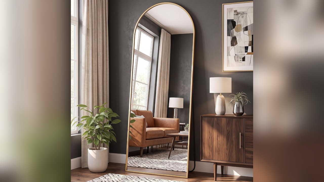 Arched full length floor mirror leaning in a bright small bedroom corner