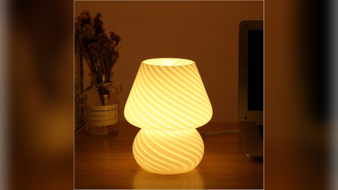 Striped glass mushroom lamp glowing warm on a bedside table in a small apartment