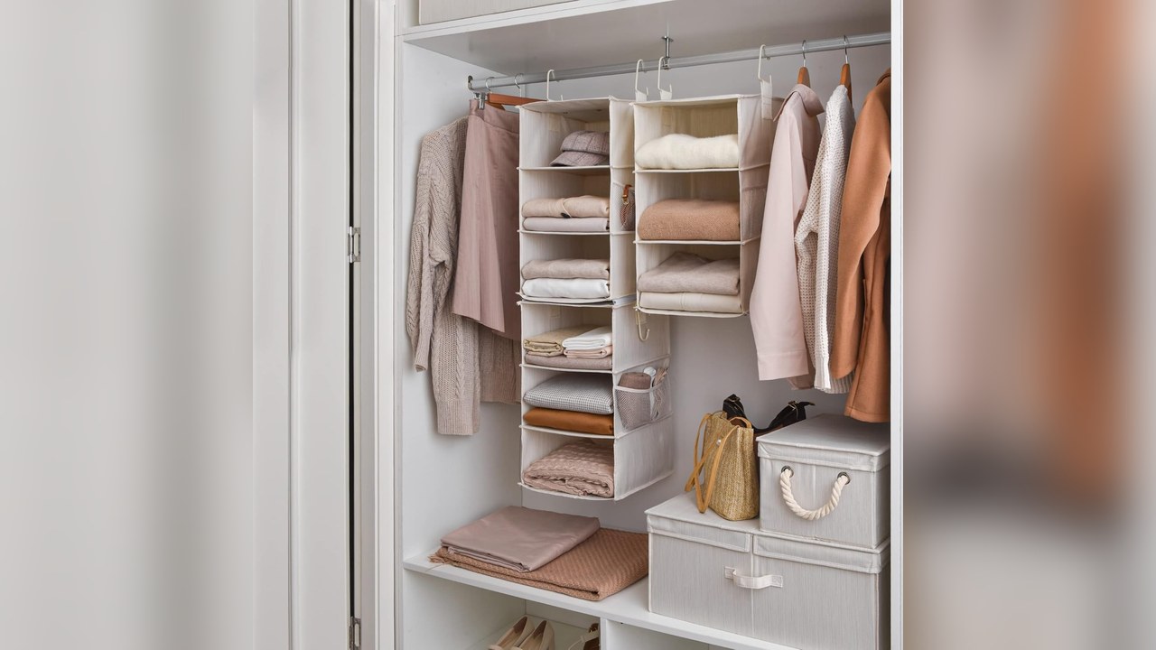 Ivory white six-shelf hanging closet organizer filled with folded sweaters and accessories in a small closet