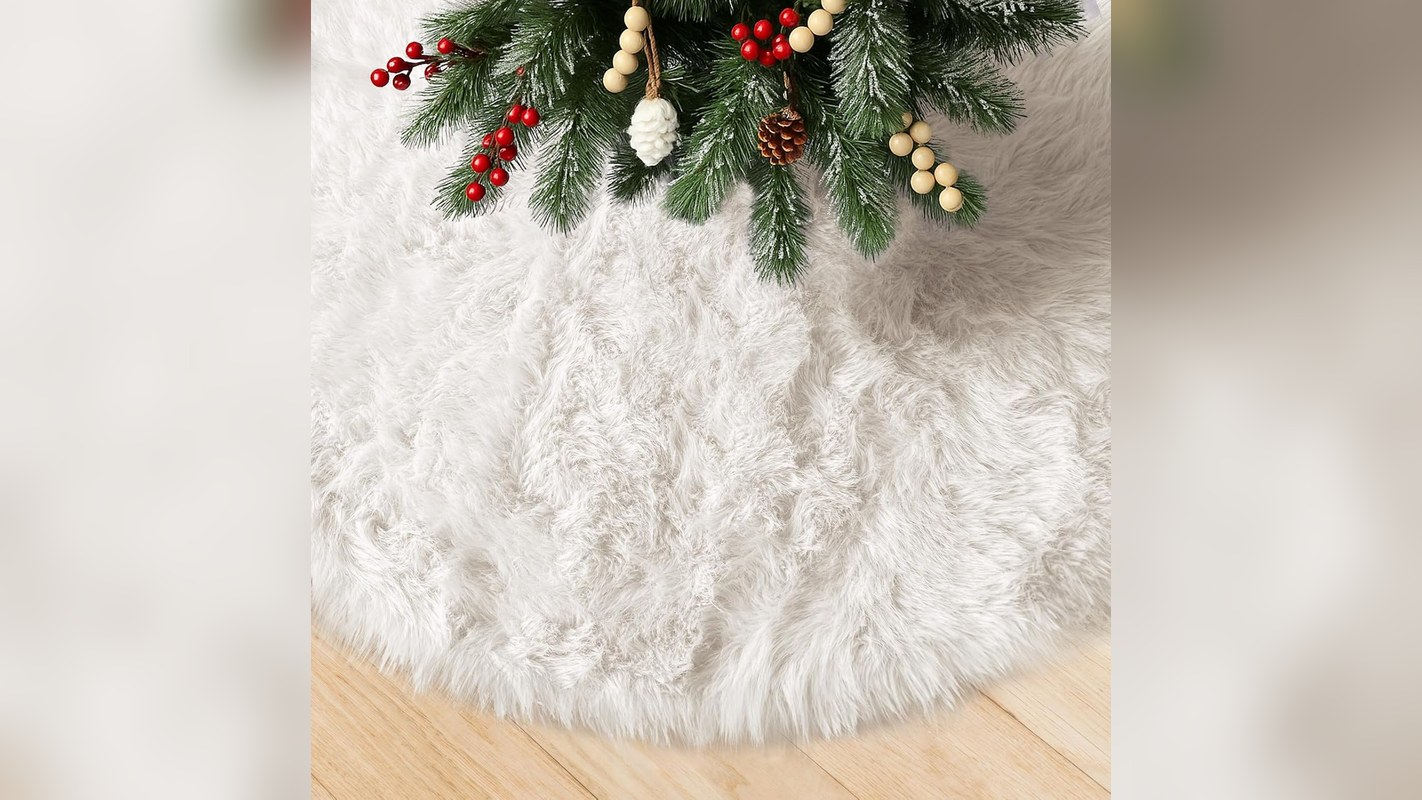 White faux fur small Christmas tree skirt spread on a wood floor under the bottom branches